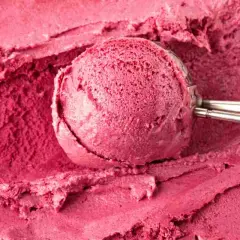 Un cucchiaio raccoglie un gelato rosa intenso, cremoso e invitante, preparato con latte e frutti di bosco.
