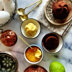 Un delizioso budino fatto in casa, pronto per essere gustato. Uova fresche, stampi in rame e una spolverata di cacao completano la scena.