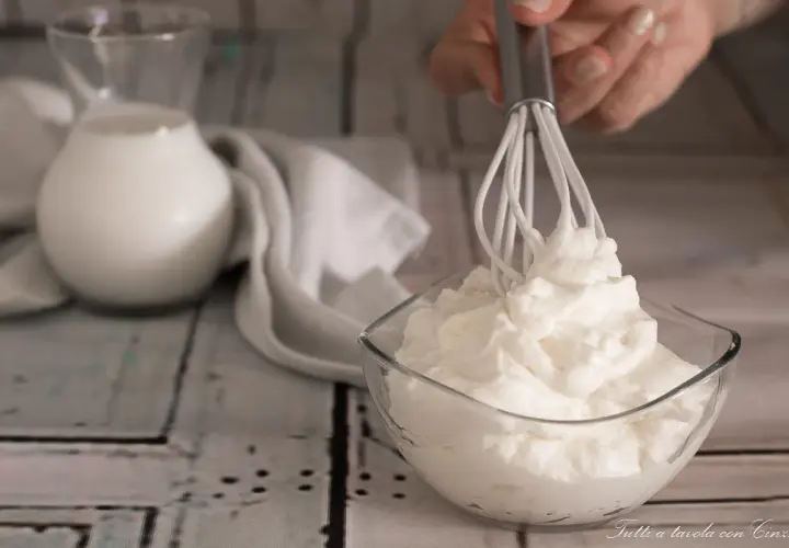 Ecco come fare la panna montata in casa: una ciotola di panna montata soffice, un frullino e una brocca di latte.