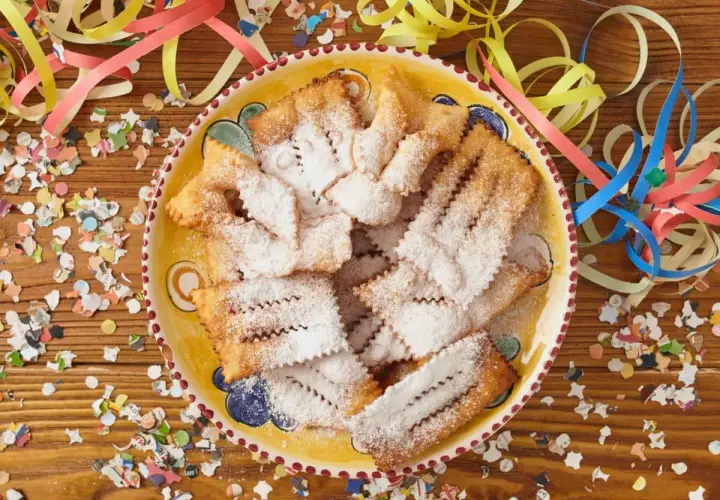 Chiacchiere di Carnevale Benedetta Rossi, cosparse di zucchero a velo, su un piatto decorato, circondate da coriandoli e stelle filanti.