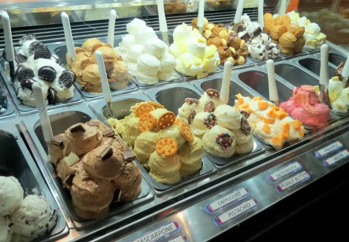 Vetrina piena di gusti di gelato, alcuni con panna montata e decorazioni golose.