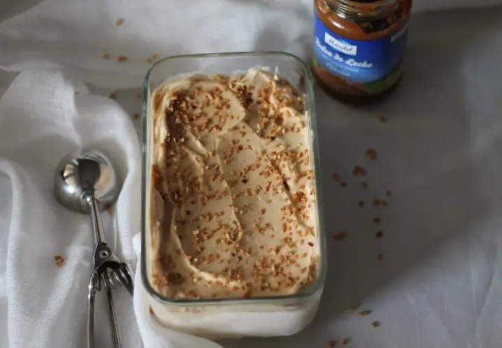 Gelato cremoso con granella di nocciole, accanto a un barattolo di dulce de leche.