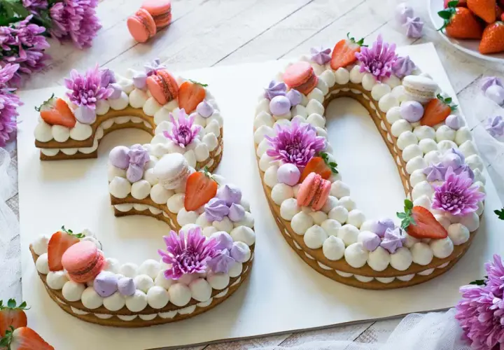 Torta numero 30 decorata con panna, fragole, macarons e fiori viola.