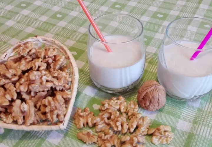 Due bicchieri con latte di noci fatto in casa, una ciotola a forma di cuore piena di noci e noci sparse sul tavolo.