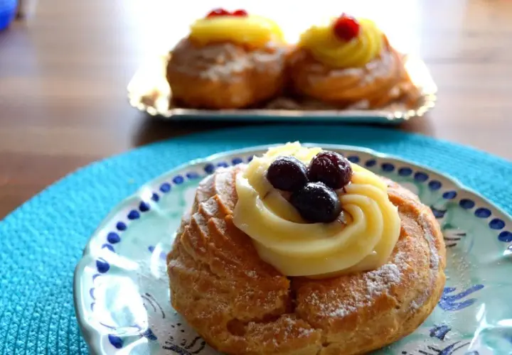 Zeppole, deliziosi dolci napoletani, guarnite con crema pasticcera e frutti di bosco su un piatto decorato.