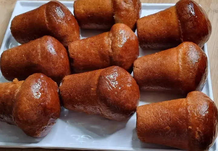 Un vassoio di baba napoletani, dolci iconici del baba Italia, dorati e lucidi di sciroppo.