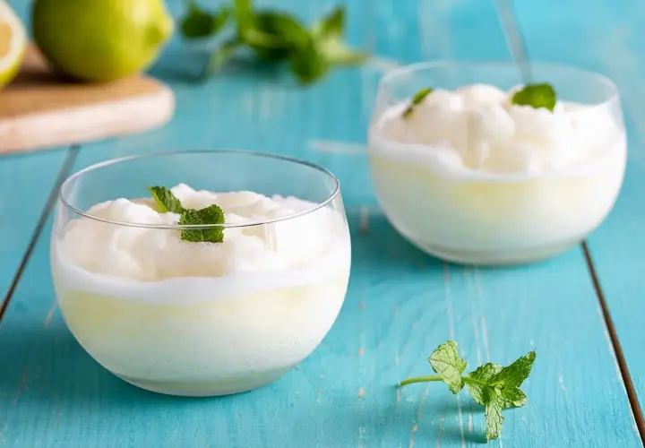 Due bicchieri di sorbetto con albume, guarniti con menta fresca, su un tavolo di legno blu.