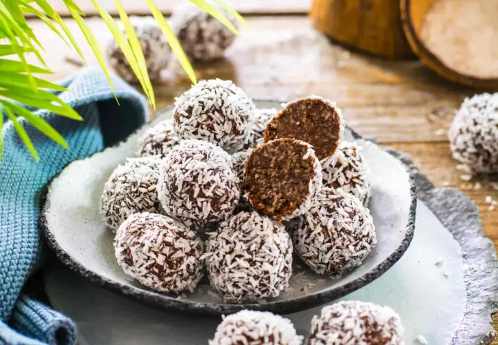Un piatto pieno di golose palline di cocco, alcune intere, altre tagliate a metà per mostrare il ripieno scuro e invitante.