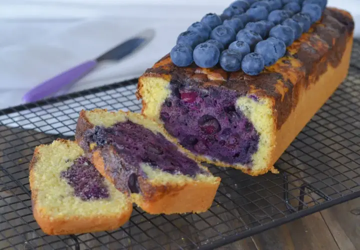 Plumcake ai mirtilli appena sfornato, con mirtilli freschi in cima e all'interno, su una griglia di raffreddamento.