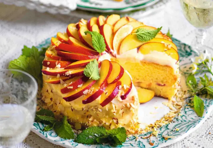 Torta di pesche morbidissima, decorata con fettine di pesca, mandorle e menta. Un dolce estivo invitante.