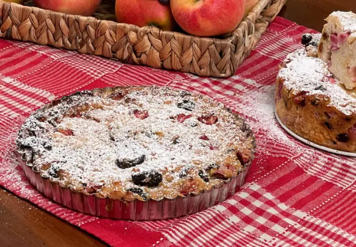 Una torta putana, ricca di frutta e spolverata di zucchero a velo, su una tovaglia a quadri rossi.