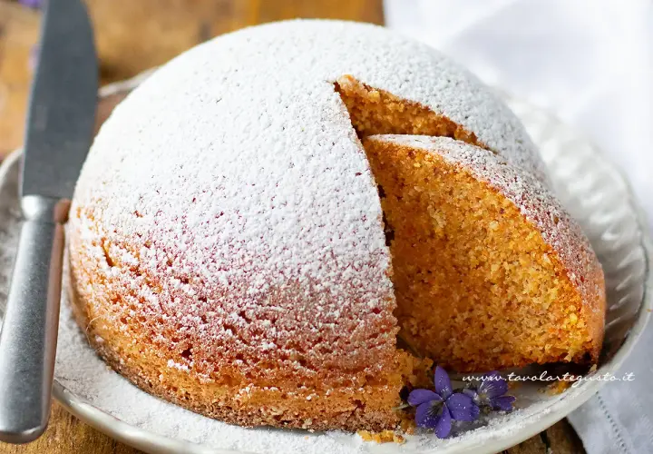 Torta Camilla ricetta originale: soffice torta cosparsa di zucchero a velo, con una fetta tagliata che rivela l'interno dorato e profumato.