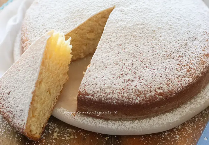 Torta soffice senza uova, cosparsa di zucchero a velo, con una fetta tagliata che ne mostra l'interno dorato.
