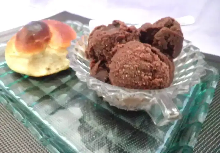 Un dolce pane intrecciato accanto a una coppa di granita cioccolato, serviti su un piatto di vetro.