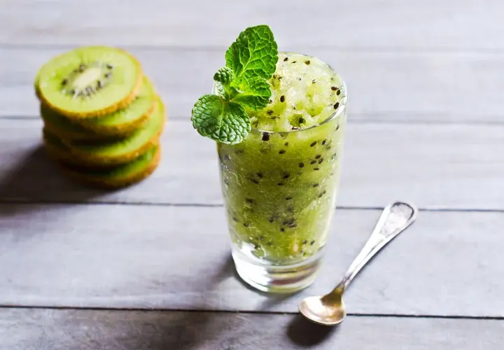 Sorbetto al kiwi rinfrescante, guarnito con menta, accanto a fette di kiwi impilate e un cucchiaino.