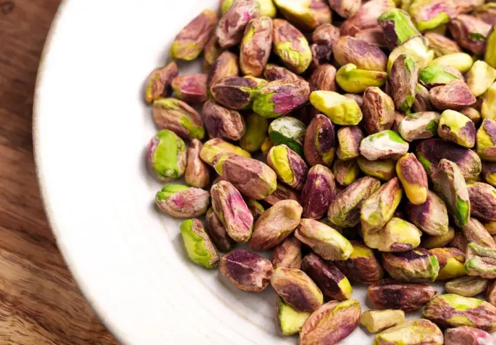 Pistacchi sgusciati su un piatto bianco, un assaggio di dove cresce il pistacchio in Italia, con i loro colori verdi e viola.