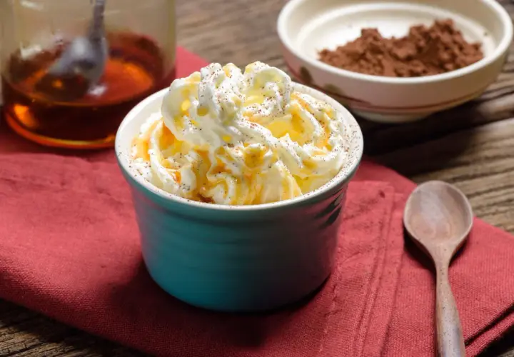 Dolcezza cremosa: cos'è heavy cream? Panna montata soffice, caramello dorato e una spolverata di cacao su un tavolo rustico.