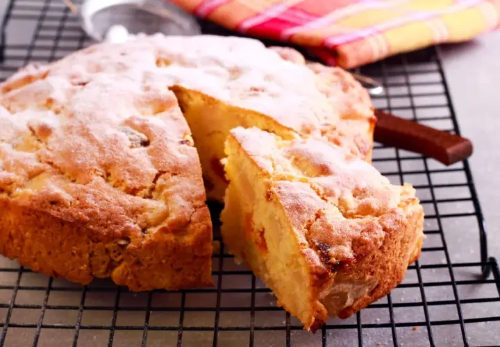 Una fetta di torta albicocche, cosparsa di zucchero a velo, riposa su una griglia.