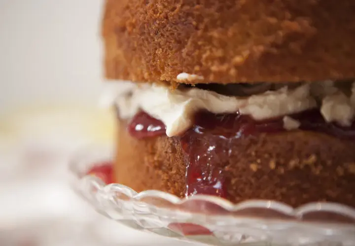 Torta soffice con panna e tanta marmellata di fragole che cola, servita su un piatto di cristallo.