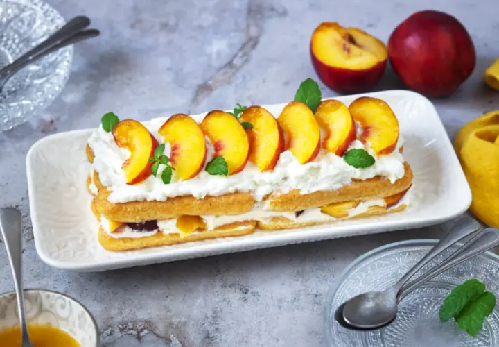 Delizioso tiramisù alle pesche, con strati di savoiardi, crema soffice e pesche fresche, guarnito con menta.