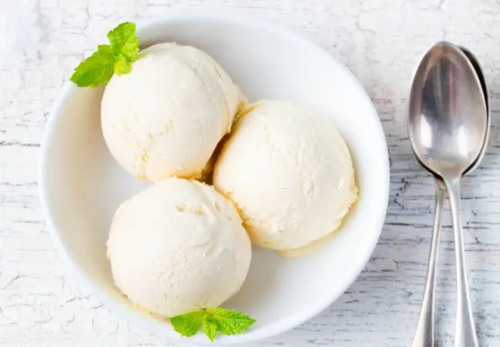 Tre palline di gelato alla vaniglia in una ciotola bianca, guarnite con menta. Perfetto per scoprire come rendere cremoso il gelato fatto in casa.