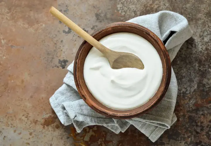 Ciotola di terracotta con panna fresca e cucchiaio di legno, un'idea su come si fa la panna da cucina in casa.