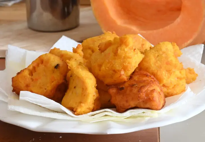 Frittelle di zucca dorate e croccanti, servite su carta assorbente, con una fetta di zucca sullo sfondo.