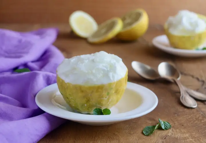 Sorbetto al limone ricetta: un fresco dessert servito in un limone svuotato, con limoni affettati e menta sullo sfondo.