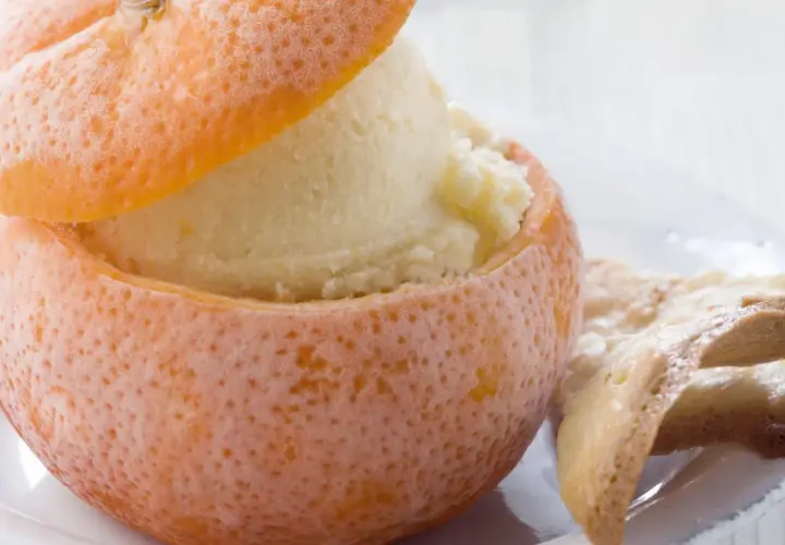 Sorbetto all'arancia servito in una scorza d'arancia ghiacciata, accompagnato da biscotti croccanti.