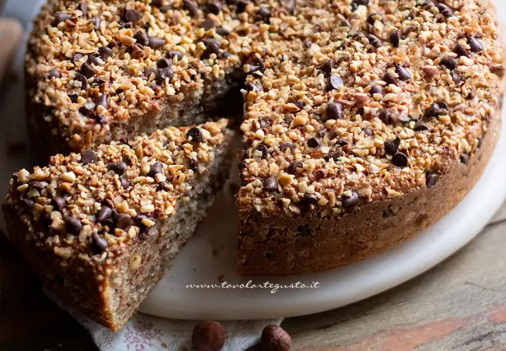 Deliziosa torta di nocciole piemontese, ricca di nocciole tritate e gocce di cioccolato, con una fetta tagliata.