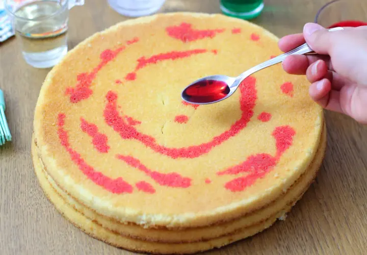 Un cucchiaino di sciroppo rosso viene versato su un pan di spagna a strati, decorato con un motivo a spirale.