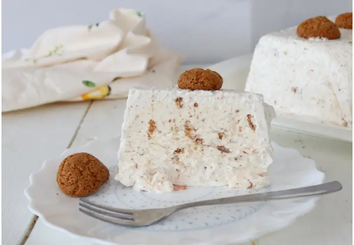 Una fetta di semifreddo agli amaretti, guarnita con un amaretto intero e un altro sul dolce intero sullo sfondo.