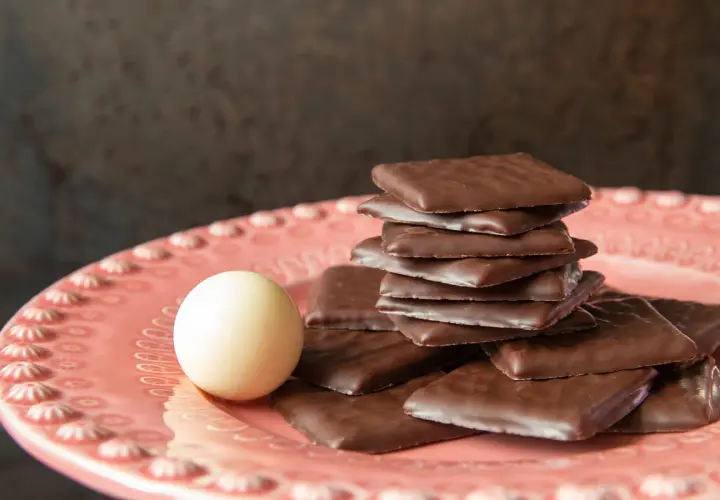 Piatto rosa con cioccolatini quadrati al cioccolato fondente e una pallina bianca. Un invito al gusto after eight.