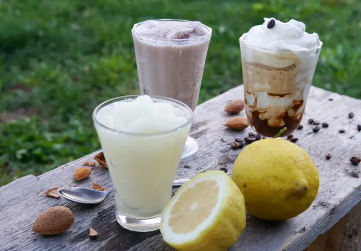 Tre granite siciliane, una al limone, preparate con gelatiera, su un tavolo di legno con limoni e mandorle.