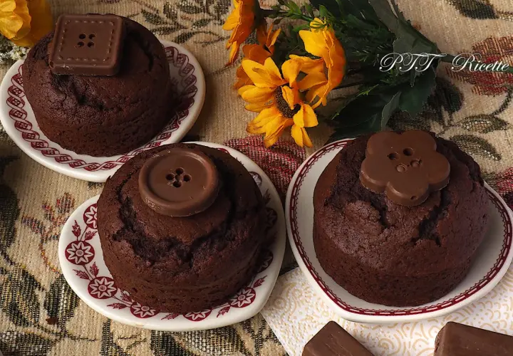 Tre deliziosi cupcake al cioccolato, decorati con bottoni di cioccolato, su piattini con fiori gialli sullo sfondo.