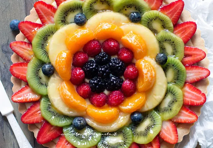 Torta alla frutta coloratissima, con fragole, kiwi, mandarini, lamponi e mirtilli disposti a raggiera su una base croccante.