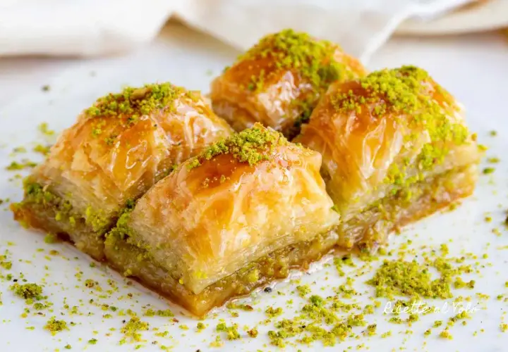 Quattro dolcetti di baklava, ricoperti di sciroppo dorato e pistacchi tritati, pronti per essere gustati.