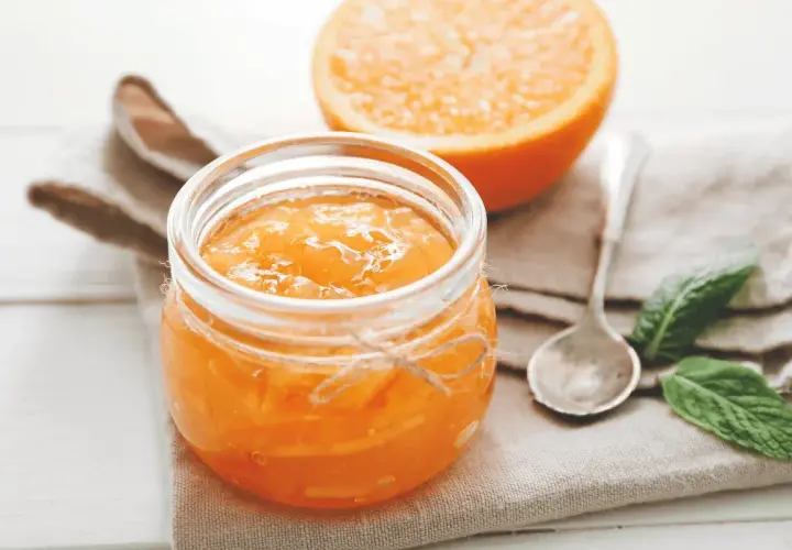 Barattolo di marmellata di arance fatto in casa, con una fetta d'arancia sullo sfondo.