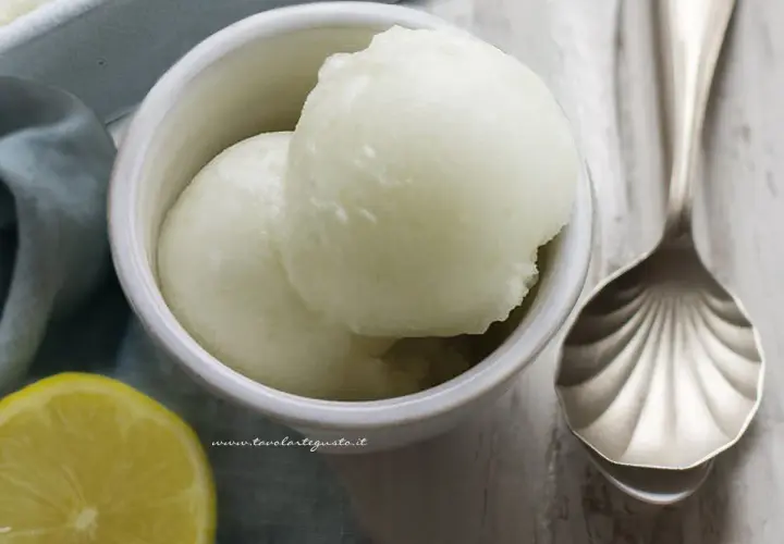 Delizioso sorbetto fatto in casa al limone, servito in una ciotola con una fetta di limone e un cucchiaio decorato.