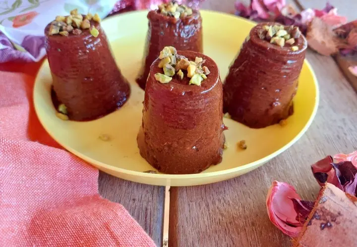 Quattro budini cachi e cacao, guarniti con pistacchi tritati, su un piatto giallo.