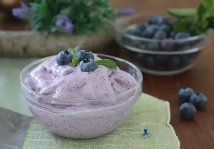 Delizioso gelato ai mirtilli fatto in casa con gelatiera, guarnito con mirtilli freschi e menta.