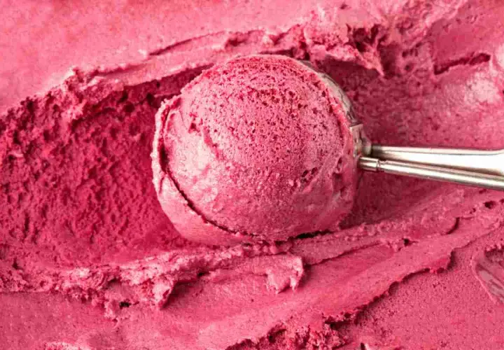 Un cucchiaio raccoglie un gelato rosa intenso, cremoso e invitante, preparato con latte e frutti di bosco.