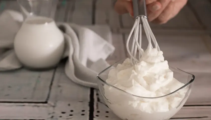 Ecco come fare la panna montata in casa: una ciotola di panna montata soffice, un frullino e una brocca di latte.