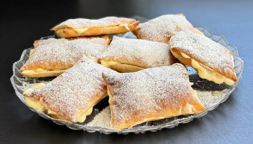 Deliziosi dolci con pasta sfoglia ripieni di crema e spolverati di zucchero a velo, serviti su un piatto di vetro.