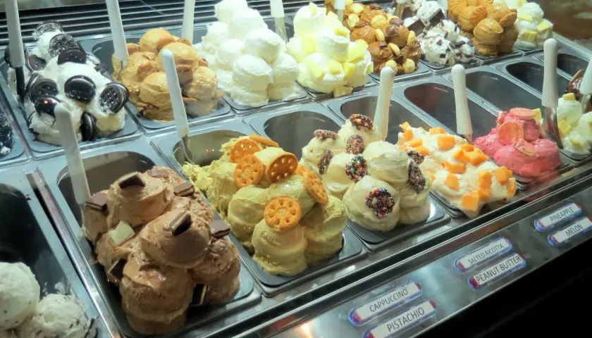 Vetrina piena di gusti di gelato, alcuni con panna montata e decorazioni golose.