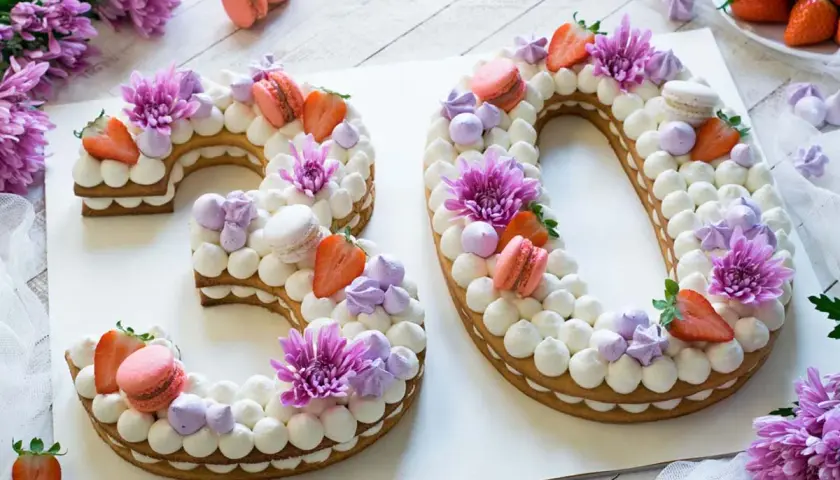 Torta numero 30 decorata con panna, fragole, macarons e fiori viola.