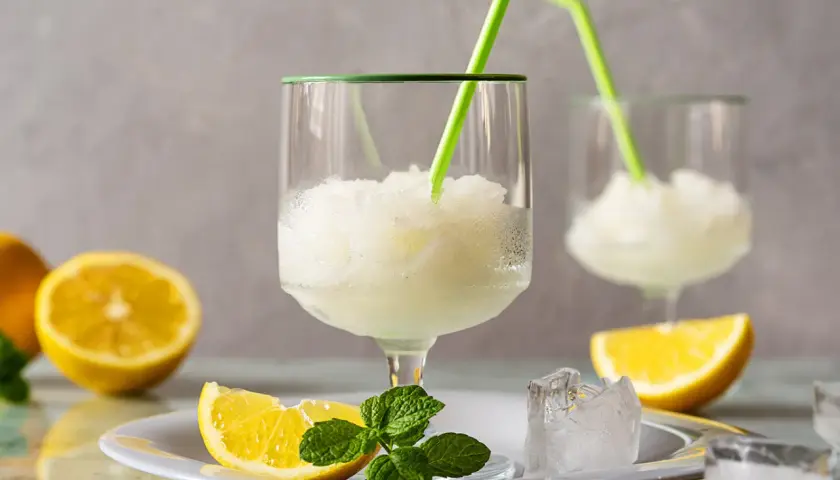 Sorbetto al limone fresco, preparato con la gelatiera, servito in bicchieri con cannucce verdi, guarnito con spicchi di limone e menta.