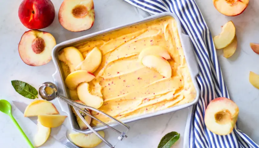 Sorbetto alla pesca fatto in casa, con pesche fresche e un cucchiaio per servirlo. Un dolce estivo rinfrescante.