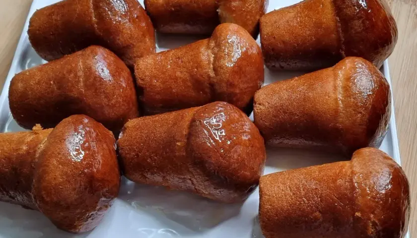 Un vassoio di baba napoletani, dolci iconici del baba Italia, dorati e lucidi di sciroppo.