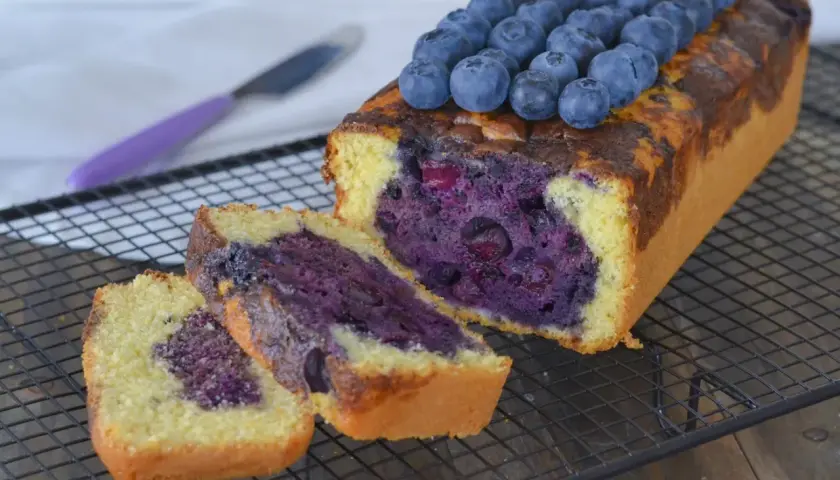 Plumcake ai mirtilli appena sfornato, con mirtilli freschi in cima e all'interno, su una griglia di raffreddamento.